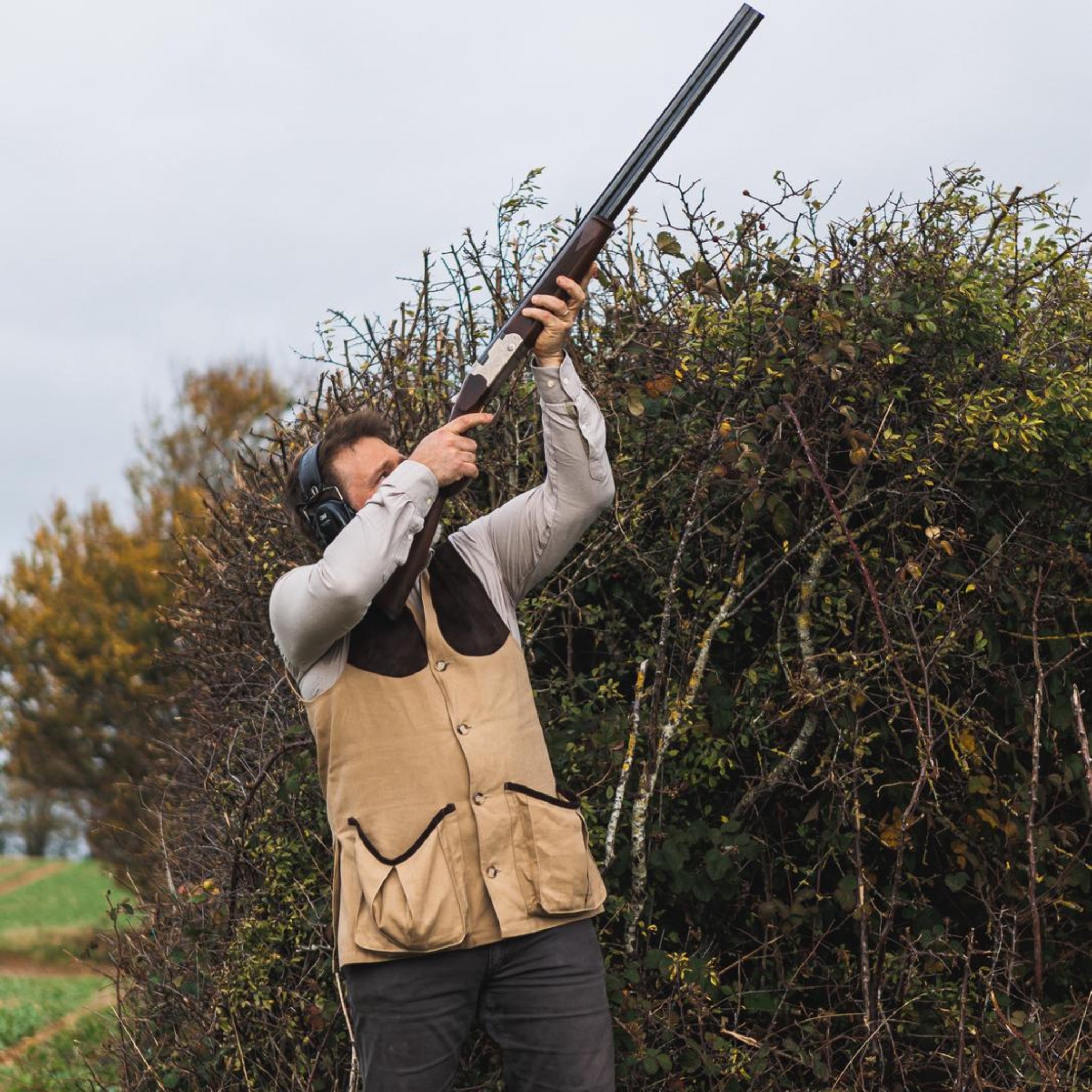 Person in hunting attire holding a shotgun in a natural outdoor setting