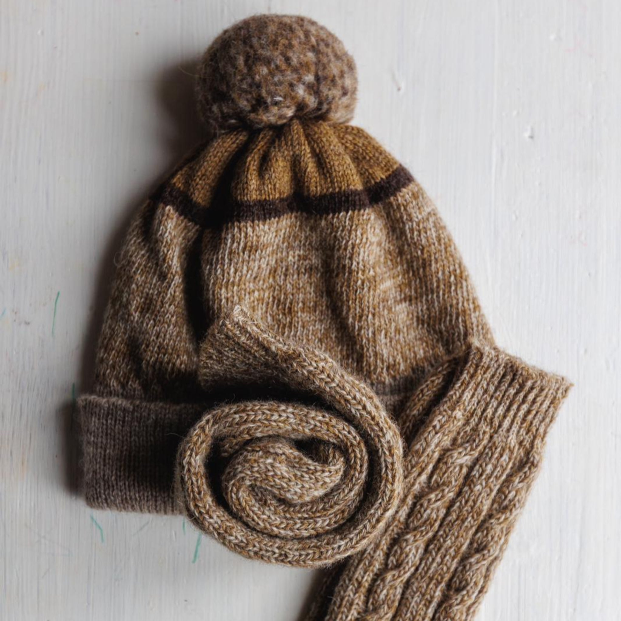 Knitted brown hat and socks curled up set on a light wooden surface